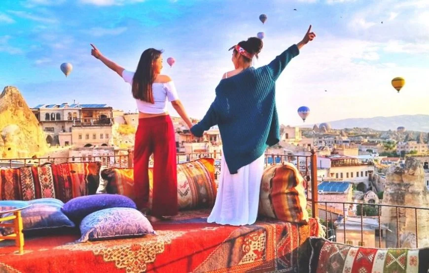 Spectators watching hot air balloon ride in Cappadocia's skyline against the dawn sky.