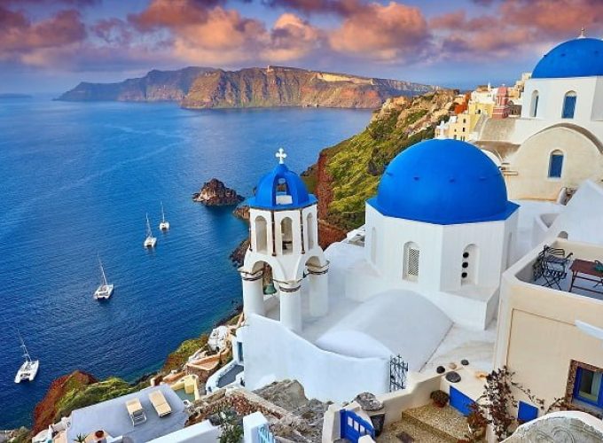 Aerial view of Mykonos town in Greece, showcasing white buildings, blue-domed churches, and a bustling harbor.