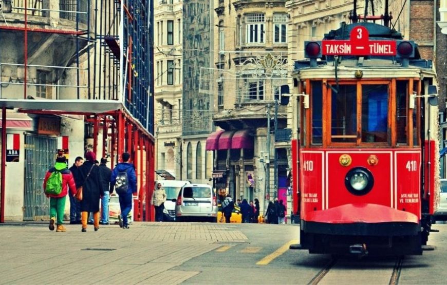 Historic red tram moving through Istiklal Street in Taksim, Istanbul, surrounded by vibrant shops and cafes.